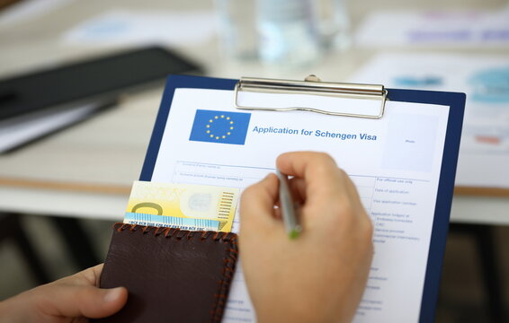 Focus on male hand holding paper folder, passport with money and answering to questions posed in application for schengen visa. Travelling abroad and immigration concept. Blurred background