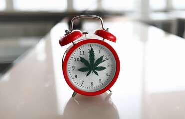 Red alarm clock with marijuana logo on office table closeup background