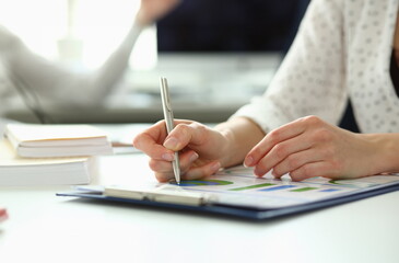 Close-up of tender female arms writing something in paper folder with important contract that can highly increase income of corporation profit. Company meeting concept