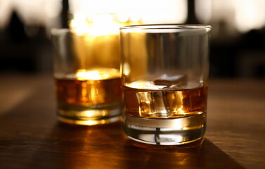 Focus on glasses of whisky or bourbon with ice-cubes. Glassful of delicious beverages on wooden table. Celebration and relax concept. Blurred background