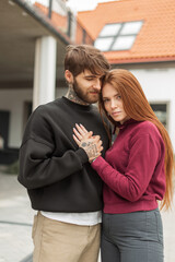 Fashionable beautiful stylish couple hugging in the city. Beautiful redhead woman and handsome hipster man with beard in fashion pullover
