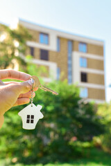 A key with a miniature house pendant in the foreground and real estate in the background.