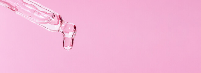 Cosmetic pipette with dripping liquid and drops on a pink background, serum, serum, gel, vitamin,...