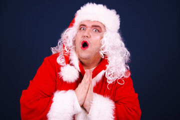 A funny drag queen enjoys life in a Santa Claus costume. Blue background.