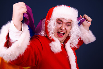 A funny drag queen enjoys life in a Santa Claus costume. Blue background.