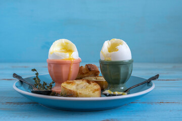 Soft boiled eggs for simple breakfast on the plate with bread pieces over blue wooden background.