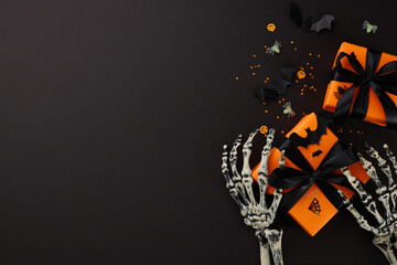 Celebrate Halloween with us. Top view flat lay of gift boxes with black ribbon and skeleton hands,...