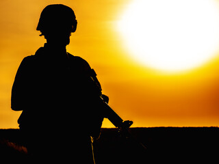 Silhouette of US soldier with rifle at sunset standing as the sun sets in the background