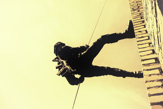 Silhouette of police officer in tactical gear descending from a height building, rope exercises with weapons. Tactical rappelling, anti-terror or counter terrorism operation in rappelling harness