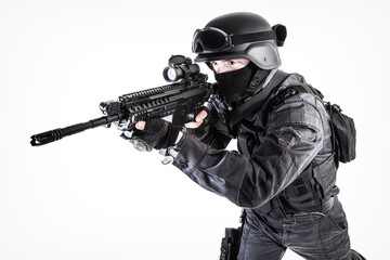 Spec ops police officer SWAT in black uniform aiming service rifle, studio shot