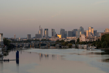 Naklejka premium Gennevilliers, France - 09 10 2023: Panoramic view of the Seine river and La Defense towers district from Clichy bridge at sunrise.
