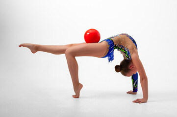 A girl gymnast in a leotard with a red ball does an exercise. White background