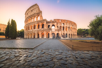 Fototapeta premium Iconic Flavian Amphitheatre, the ancient Roman Colosseum, a famous tourist landmark illuminated at twilight and dawn in historic Rome, Italy.