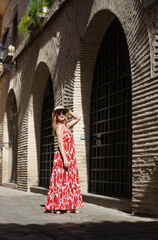 Fototapeta na wymiar Young and beautiful blonde woman with sunglasses and straw hat on her head walking in the historical centre of seville. The woman is on holiday and enjoys the city. The woman is happy.