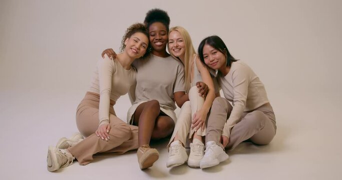 attractive women with different appearance, nationalities sitting together in studio Slow motion, Different skin types Beauty beige background Cheerful multiracial female friends laughing, having fun