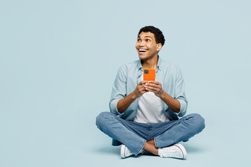 Full body happy young man of African American ethnicity wear shirt casual clothes sit hold use...