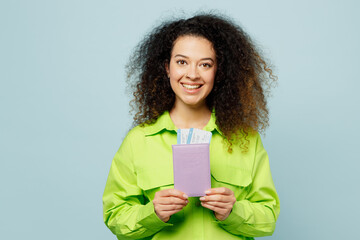 Traveler latin woman wears green casual clothes hold passport ticket isolated on plain pastel blue background. Tourist travel abroad in free spare time rest getaway. Air flight trip journey concept.