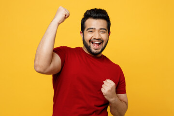 Young excited happy Indian man he wears red t-shirt casual clothes doing winner gesture celebrate...