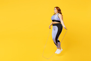 Fototapeta na wymiar Full body side profile view young chubby plus size big fat fit woman wears blue top warm up training jumping on skipping rope isolated on plain yellow background studio home gym Workout sport concept