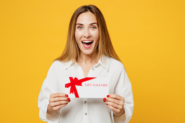 Young excited surprised shocked happy woman wears white shirt casual clothes hold gift certificate coupon voucher card for store isolated on plain yellow background studio portrait. Lifestyle concept.