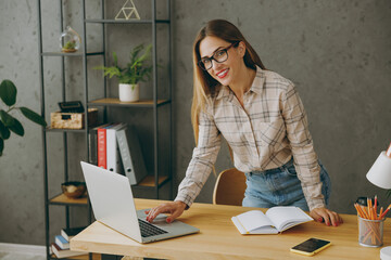 Young successful confident fun caucasian entrepreneur employee business woman wear shirt casual clothes glasses work stand near office desk with pc laptop, look camera. Achievement career job concept.