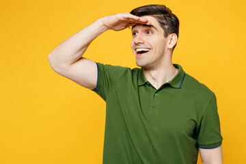 Young smiling fun cool happy caucasian man he wearing green t-shirt casual clothes hold hand at forehead look far away distance isolated on plain yellow background studio portrait. Lifestyle concept.