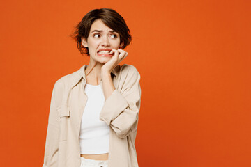 Young sad mistaken displeased caucasian woman she wears beige shirt casual clothes look aside on area biting nails fingers isolated on plain orange red background studio portrait. Lifestyle concept.