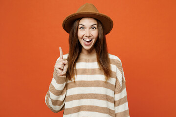 Young proactive woman she wears striped sweater hat casual clothes holding index finger up with great new idea isolated on plain orange red color wall background studio portrait. Lifestyle concept.