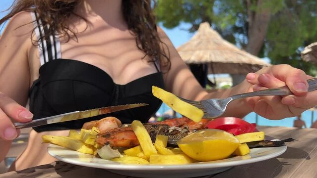 food on the beach chic restaurant in Albanian resort Ksemil a girl eats fish and fries with knife and fork young woman sits in shade eats seafood large shrimp and Dorado fish. spend time on vacation