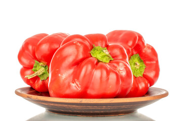 Three red sweet peppers on a clay plate, macro, isolated on white background.