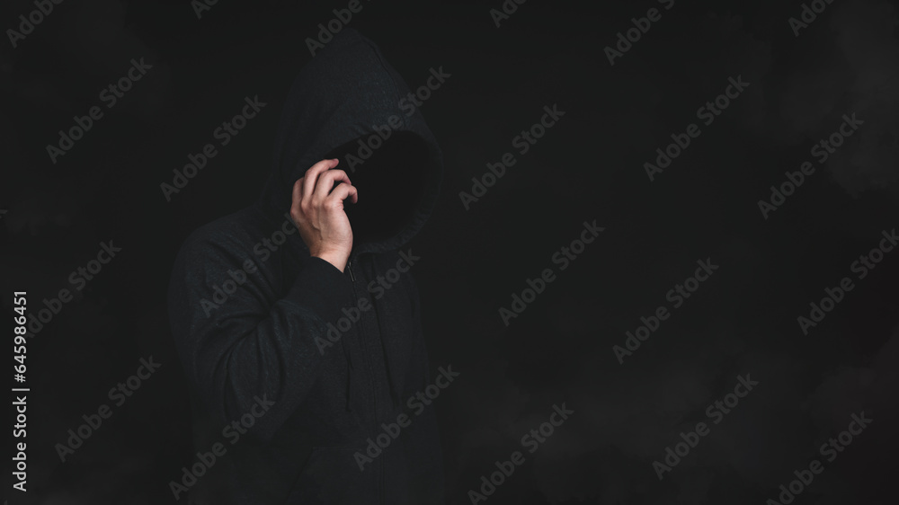 Poster an unknown man in hood jacket using cellphone in dark background. hacker, scammer or criminal using 