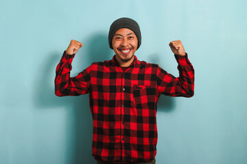Excited Young Asian man making a strong gesture, isolated on a blue background