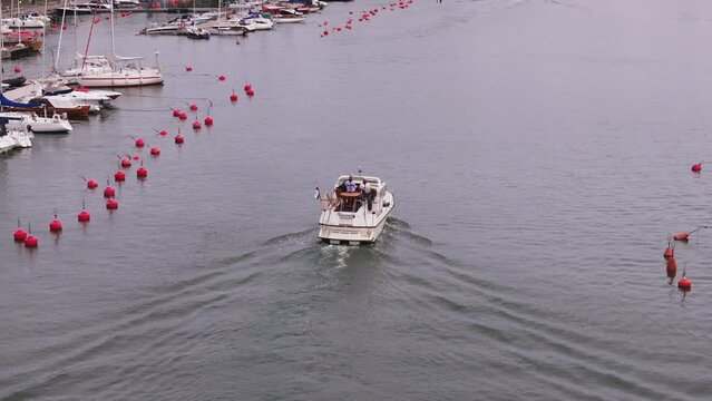 Back view of motorboat with Finnish flag sailing through port. Row of red buoys on water surface. Helsinki, Finland