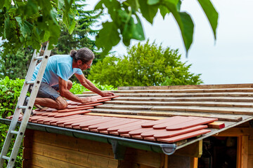 Roofer at work, installing clay roof tiles. back garden with shed, summer house garden timber...