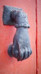 Aldabón con forma de mano en puerta de madera roja