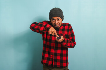 Angry young Asian man is arguing with the TV, isolated on a blue background