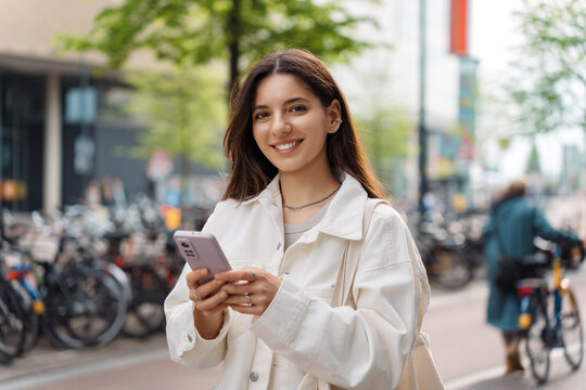 Mixed-race LGBT proud and confident Turkish young woman holding a phone in the street smiling wearing white casual clothes © Andrei