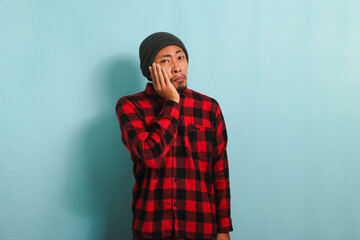 Unhappy Young Asian man holding his cheek suffering from toothache, isolated on blue background