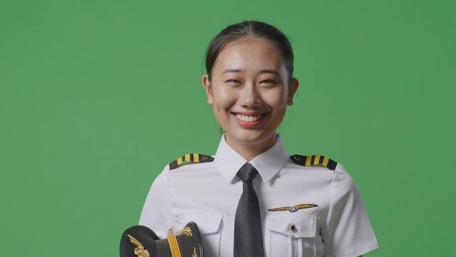 Asian Woman Pilot In Professional Uniform Launching Paper Plane, Holding Jet Model In Hands, Aviation Academy Aviator, Aircraft Captain On Green Screen Background Studio
