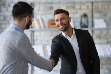 Smiling young businessmen shake hands get acquainted greeting at office meeting, happy motivated male business partners handshake closing dal or making agreement at briefing, partnership concept
