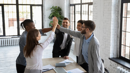 Excited multiracial colleagues give high five celebrate shared company group win or victory at...