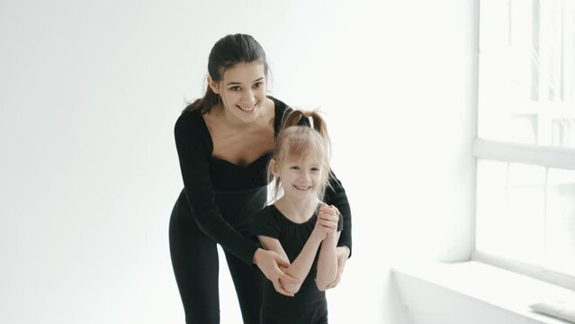 Professional cherleading trainer dancing with little girl, moving synchronically at dance class