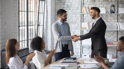 Young Caucasian boss shake hand of male employee, congratulate with job promotion at meeting, confident businessman handshake worker, greeting with employment, get acquainted at team briefing