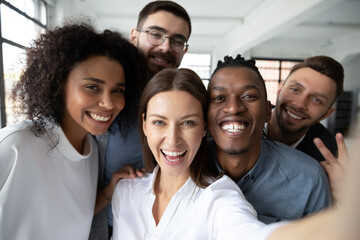 Close up of happy diverse multiracial colleagues have fun make self-portrait picture on cell at...