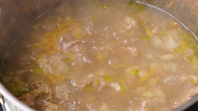 Cooking beef broth in a saucepan with boiling water closeup with seasonings and vegetables