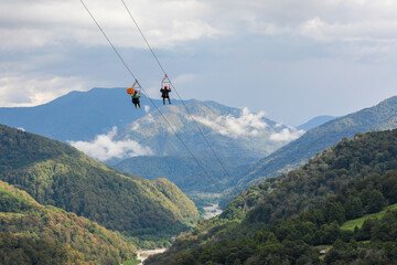 Two tourists going down on a zipline, against the backdrop of a picturesque mountain landscape. Sochi, Solokhaul, Russia.