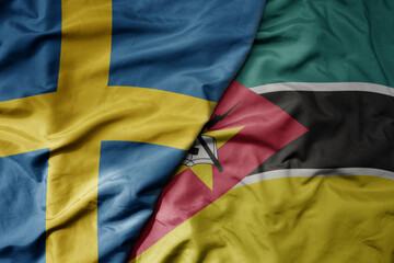 big waving national colorful flag of sweden and national flag of mozambique .
