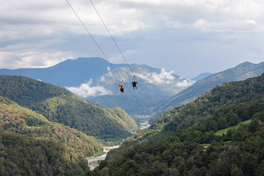Two tourists going down on a zipline, against the backdrop of a picturesque mountain landscape. Sochi, Solokhaul, Russia.