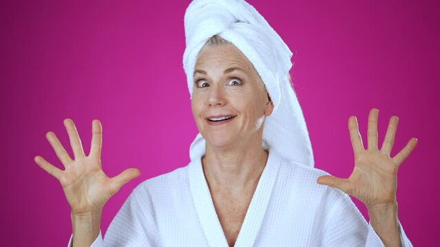 Smart pretty elderly blonde woman lady 50s years old wears white robe and towel on head, show mind explosion isolated on solid pink background studio portrait. People emotions lifestyle concept