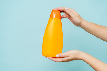 Woman's hand holding packaging of shampoo or conditioner on blue background. Copy space and mock up
